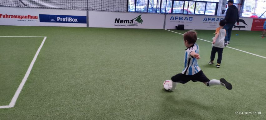 Junger Fußballspieler tritt den Ball in einem Indoor-Fußballfeld.